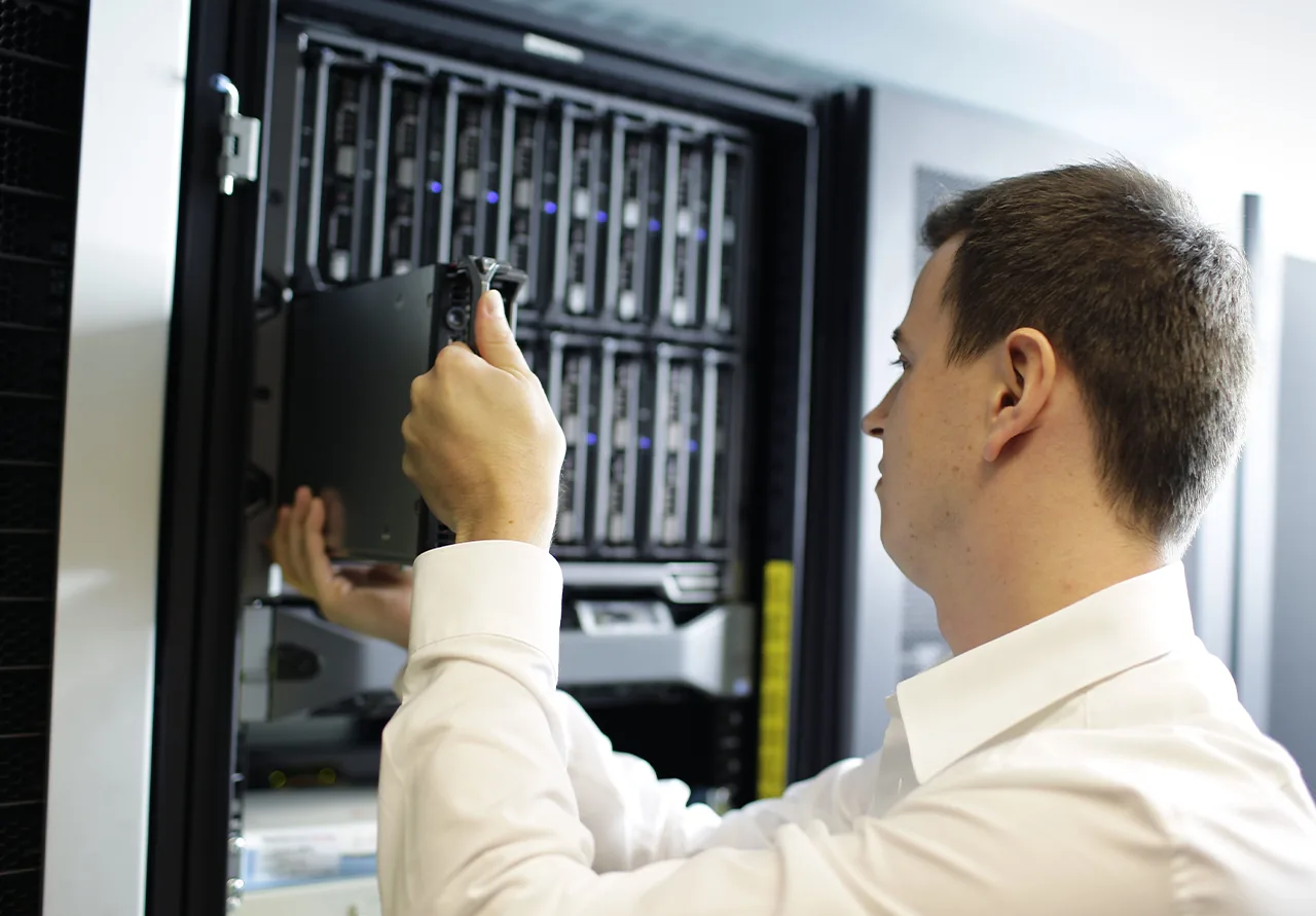 Eine Person in einem weißen Hemd baut eine Festplatte in einem Serverrack in einem Rechenzentrum ein oder aus.