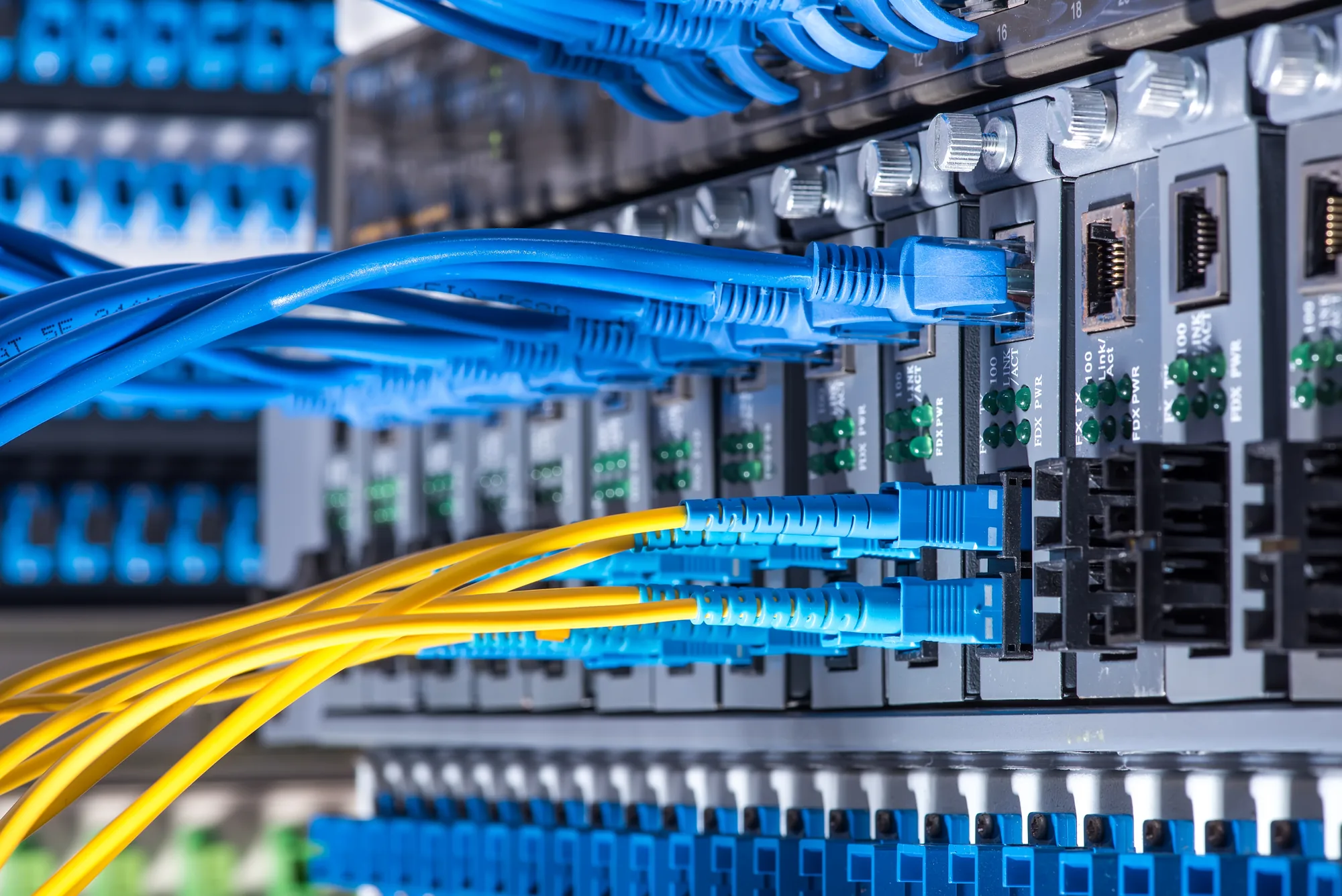 Nahaufnahme der Hardware eines Netzwerkservers mit blauen Ethernet-Kabeln und gelben Glasfaserkabeln, die an verschiedene Anschlüsse in einem Rechenzentrum angeschlossen sind.