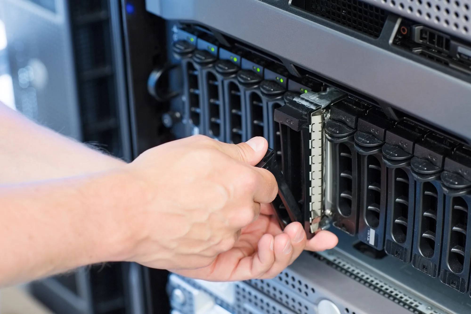 Die Hände einer Person bauen eine Festplatte in einem Server-Rack in einem Rechenzentrum ein oder aus. Der Server verfügt über mehrere Festplatteneinschübe, von denen bei einigen Kontrollleuchten zu sehen sind.